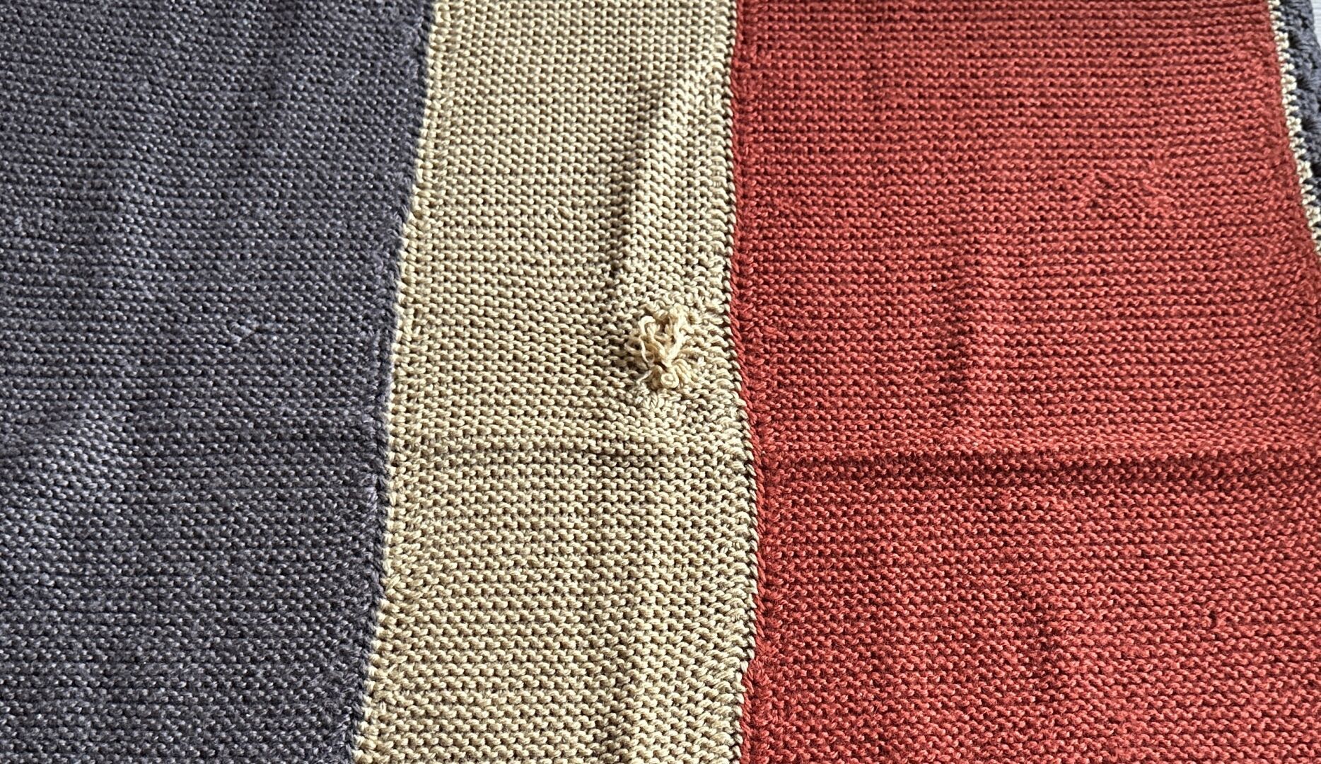 A closer view of the right mustard panel with the inexpertly mended hole. It looks messy, the fabric is pulled together and yarn ends are sticking out.