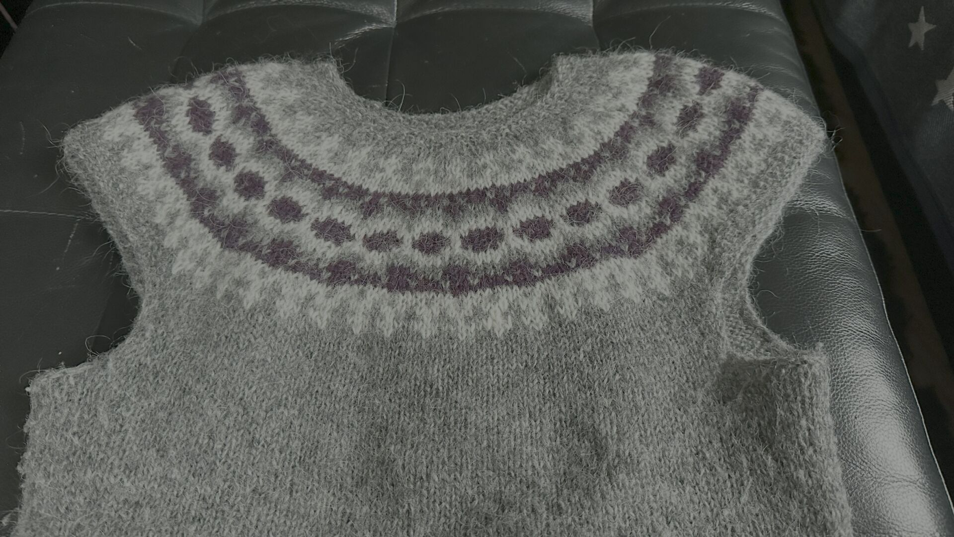 Top part of a gray vest with a patterned yoke in dark red, gray and white on a black leather background. I mended some stitches in the lower white part. It blends in quite well and isn't obvious.